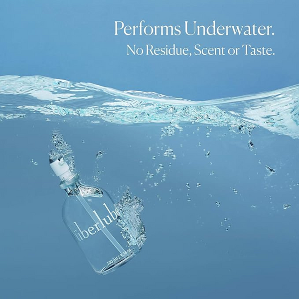 A clear glass Überlube bottle, angled downwards, is partially submerged in sparkling blue water, with bubbles rising around it. The text "Performs Underwater. No Residue, Scent or Taste." highlights the versatility of this WorldCondoms lubricant.