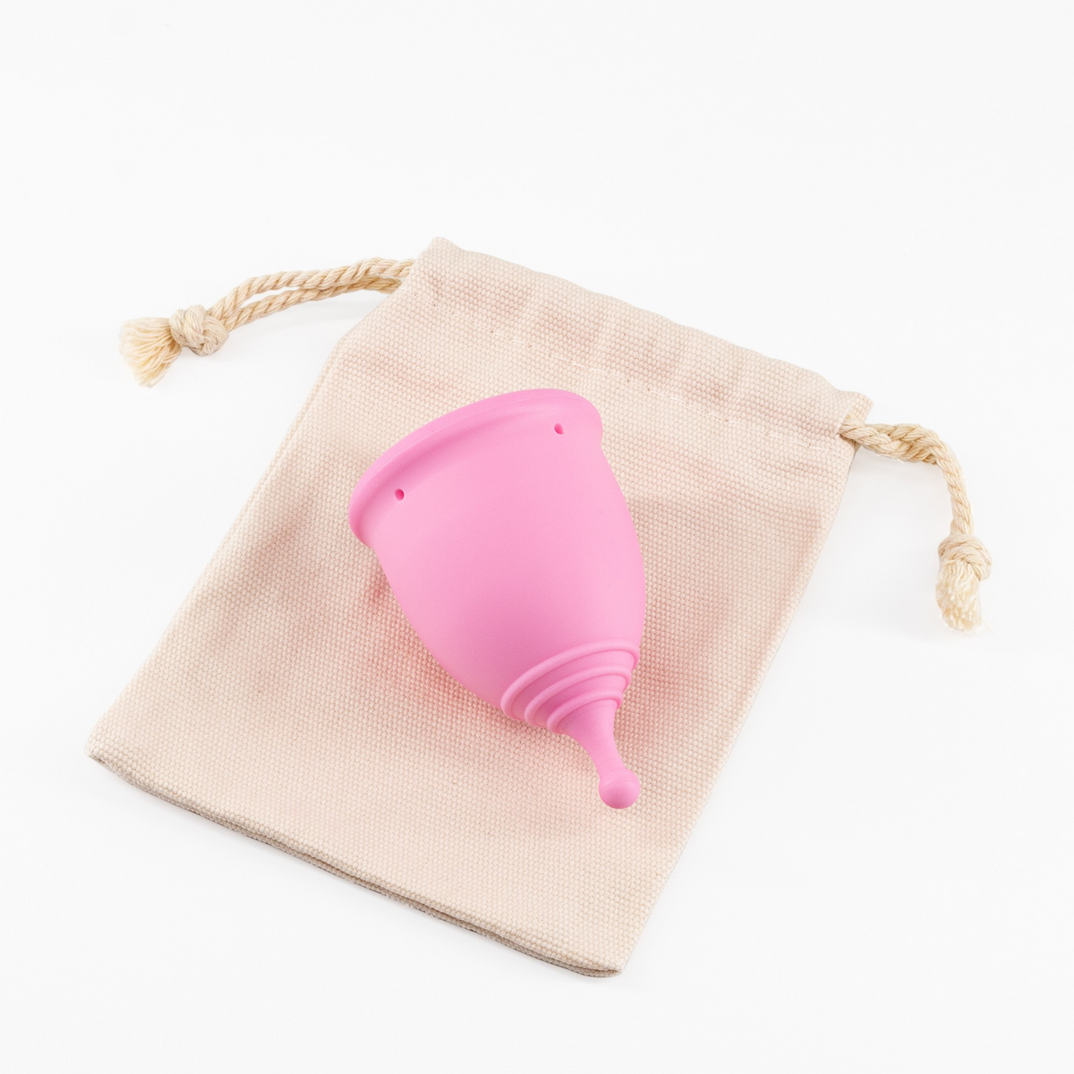 A pink menstrual cup resting on a light beige drawstring storage bag.