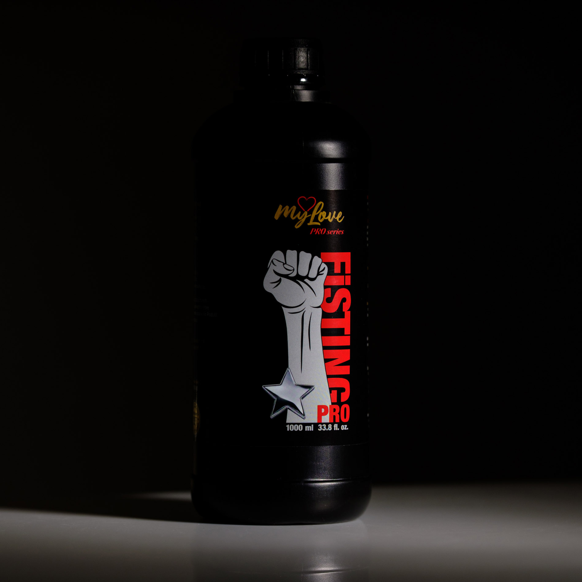 Dramatic moody lighting shot of the 1000 ml MyLove Fisting Pro Gel bottle set against a pitch-black background, with soft light illuminating the front label details and white surface underneath.