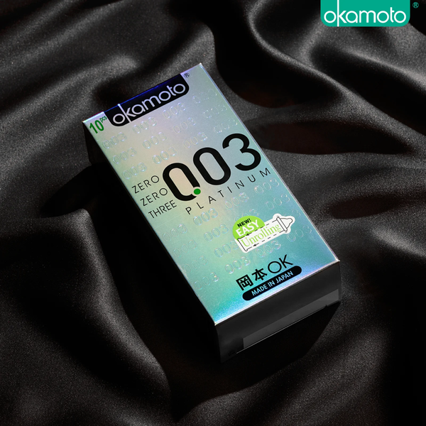 A shot of a Okamoto 003 Platinum 10-piece box resting on luxurious black silk fabric. The box features a holographic silver finish with the signature '003' logo. A bright green sticker on the front highlights the "New! Easy Unrolling" feature.