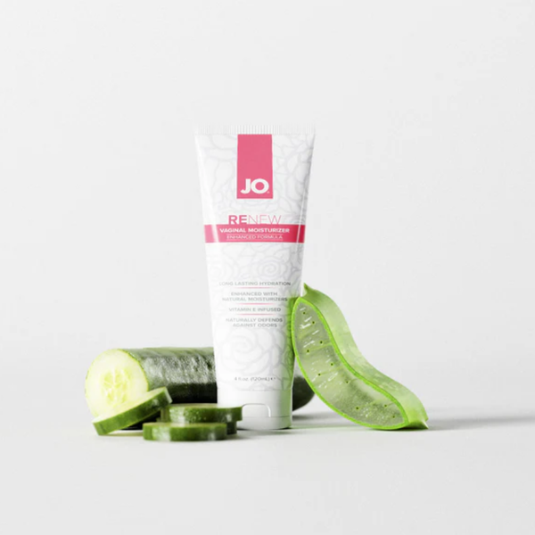 The JO Renew Vaginal Moisturizer tube stands upright on a clean, light grey surface, creatively staged next to fresh cucumber slices and a cut piece of a green aloe vera leaf to highlight its natural ingredients.