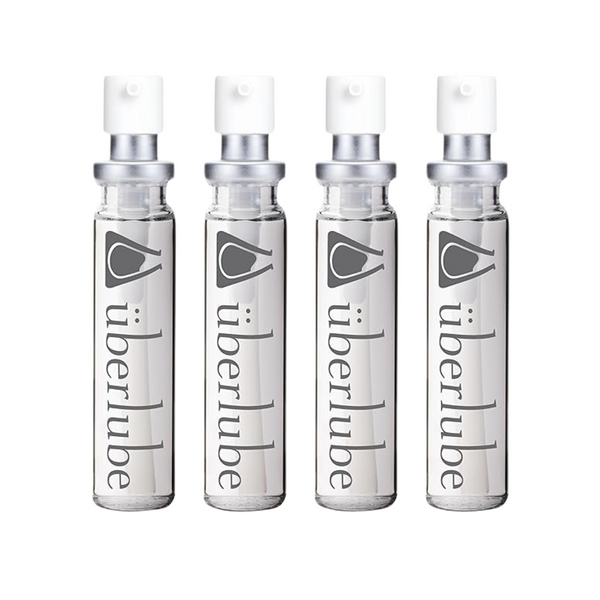 Four transparent glass spray bottles of Überlube lubricant, each with "überlube" and a stylized eye logo printed vertically, stand in a row. These travel-friendly WorldCondoms offerings provide discreet, on-the-go intimacy.