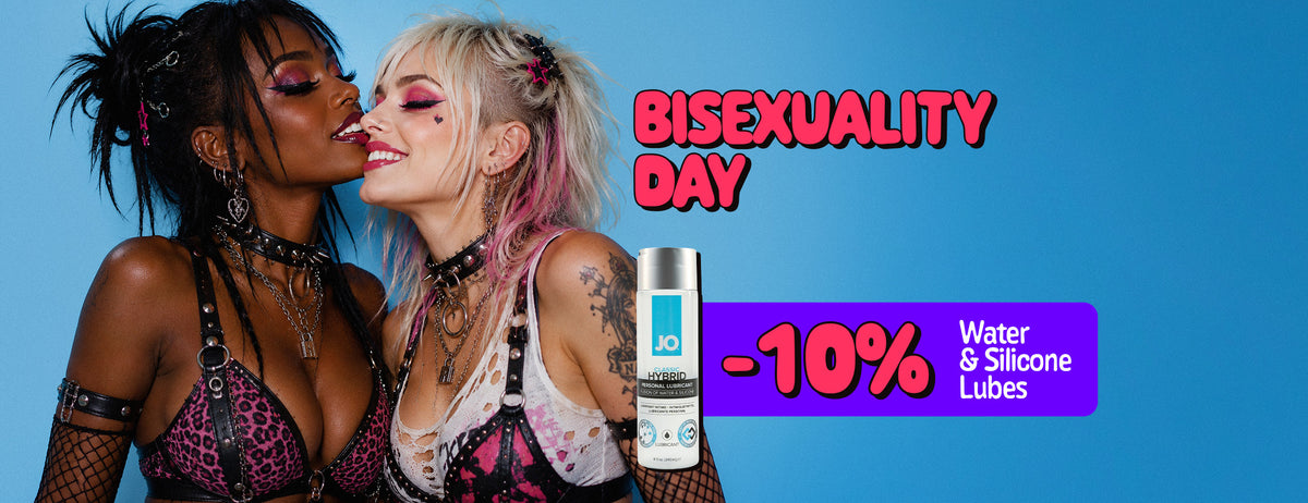 Promotional poster for Bisexuality Day. Two women in colorful alternative-style outfits and makeup pose closely together against a blue background, smiling with their faces touching. A purple promotional banner advertises “-10% Water & Silicone Lubes”, alongside an image of a personal lubricant bottle.