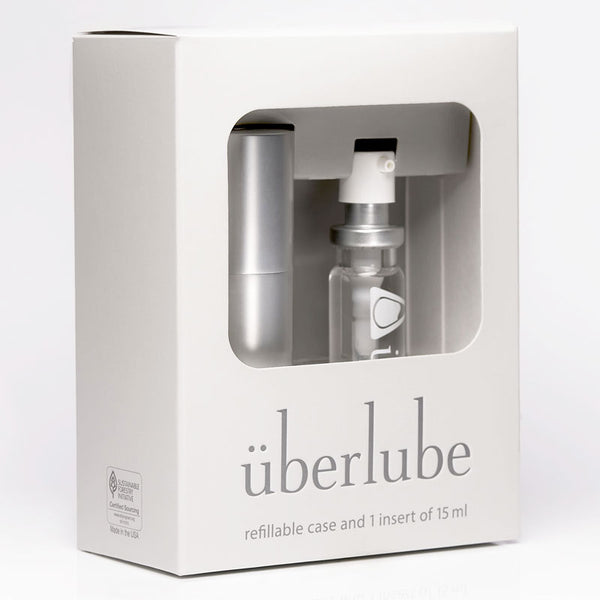 
A white box for "überlube" displays a silver refillable case and a 15ml clear insert of lubricant through a cutout. The packaging indicates "refillable case and 1 insert of 15 ml" and is available at Worldcondoms.